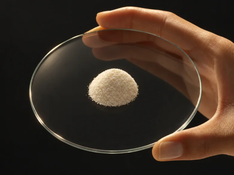 A hand holding a glass dish with a small mound of white powder